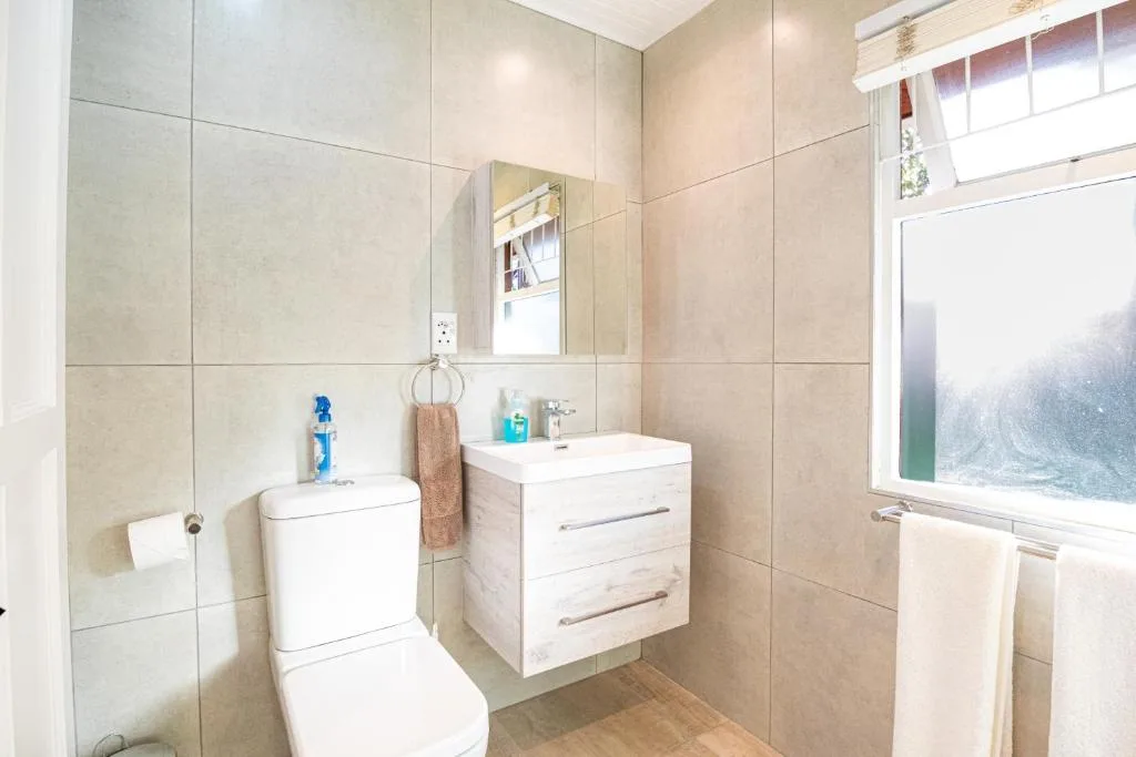 Modern bathroom with beige tiles, white vanity, toilet, and mirror