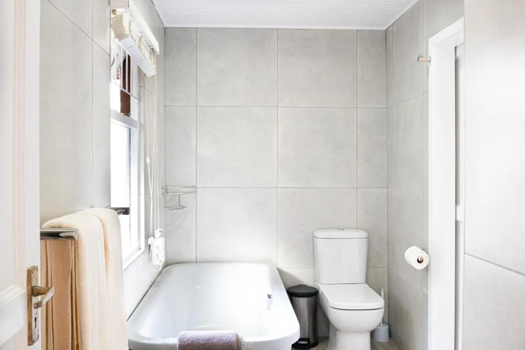 Clean white bathroom with bathtub, toilet, and window light