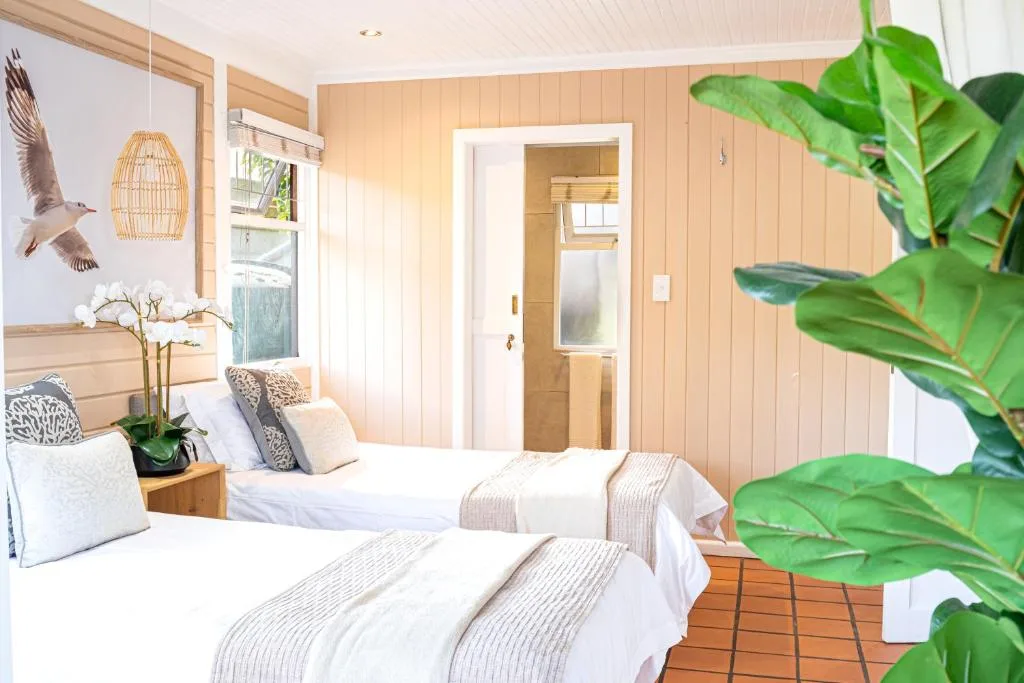 Bright bedroom with two beds, wooden walls, potted plants, and garden views