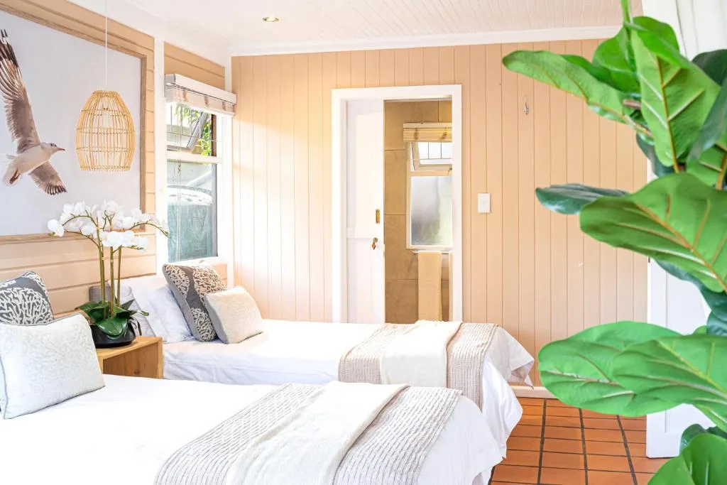 Bright bedroom with two beds, wooden paneling, potted plants, natural light