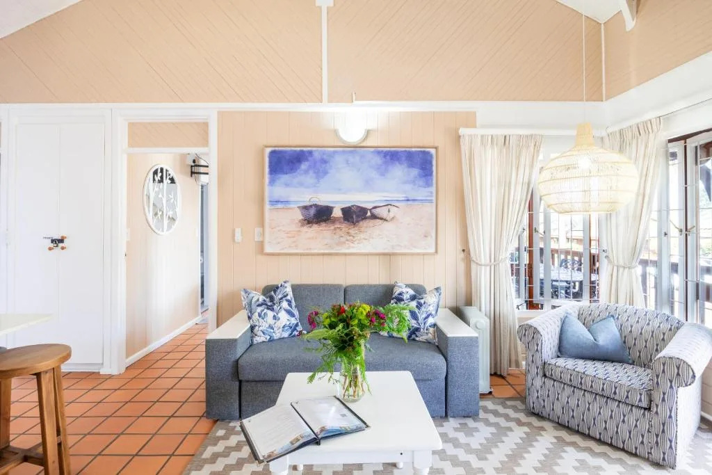 Bright open-plan lounge with grey sofa, coastal artwork, and ocean-view doors