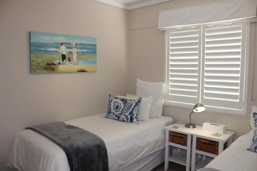 Bright bedroom with twin beds, coastal artwork, and shuttered windows