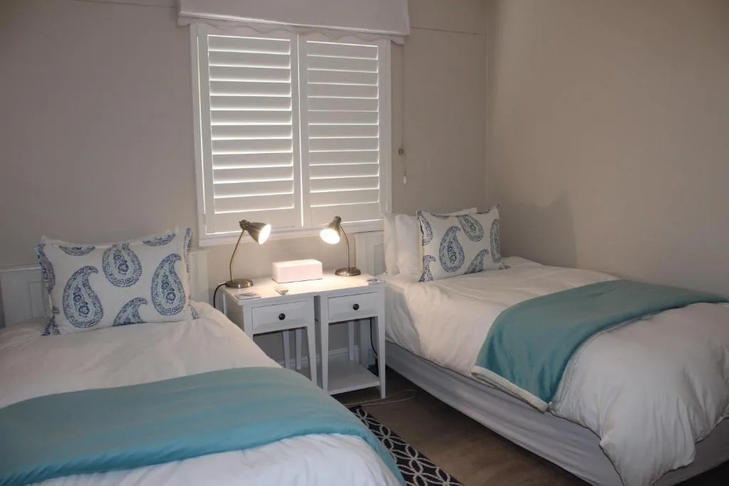 Twin bedroom with white shutters, blue patterned pillows, and bedside lamps
