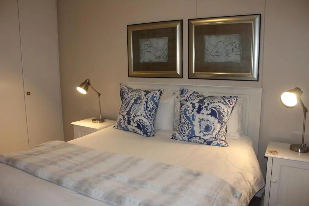Modern bedroom with white linens, blue patterned pillows, framed artwork above headboard