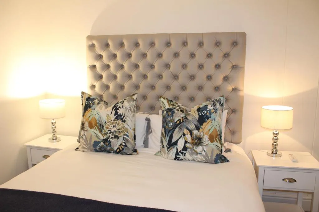 Master bedroom with upholstered headboard, floral cushions, and bedside lamps