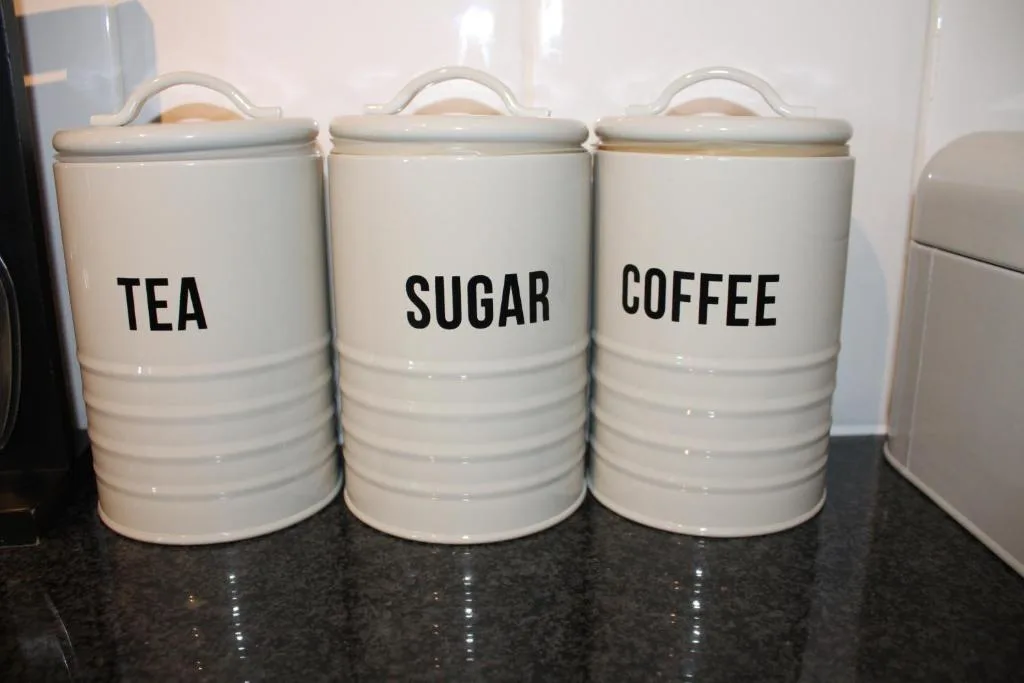 Three ceramic storage canisters labeled tea, sugar, and coffee on kitchen counter