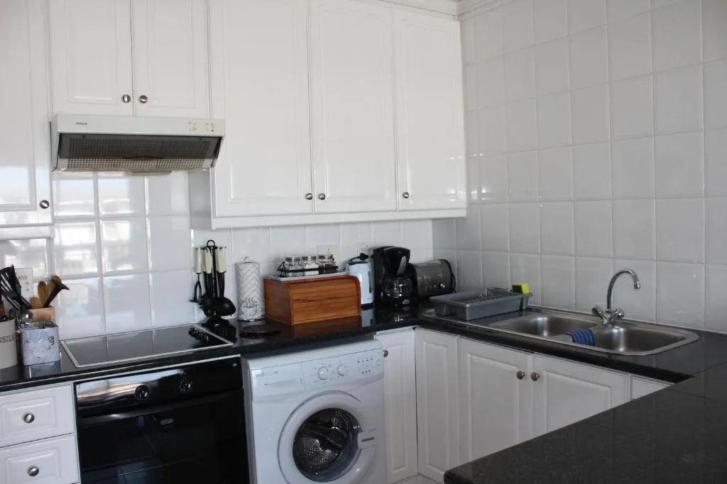 Compact white kitchen with stove, washing machine, and dark countertops