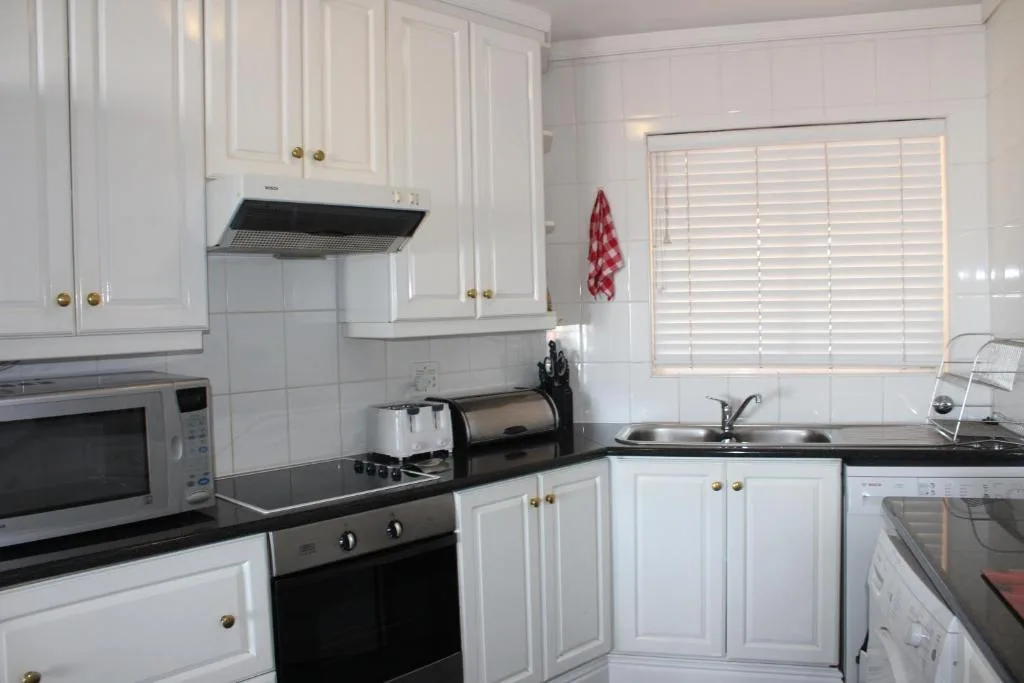 Bright white kitchen with black countertops, stainless steel appliances, and sink