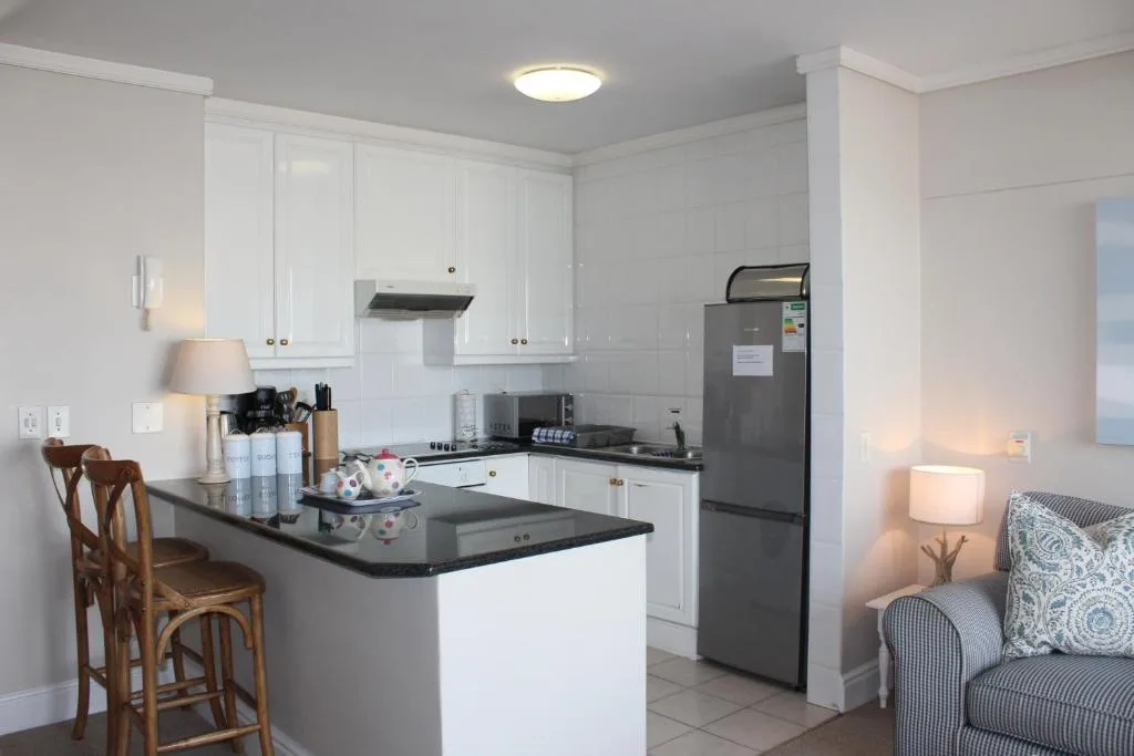 Modern white kitchen with black countertops, stainless steel appliances, and island seating