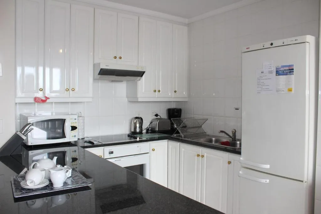 Compact white kitchen with black countertops, appliances, and storage