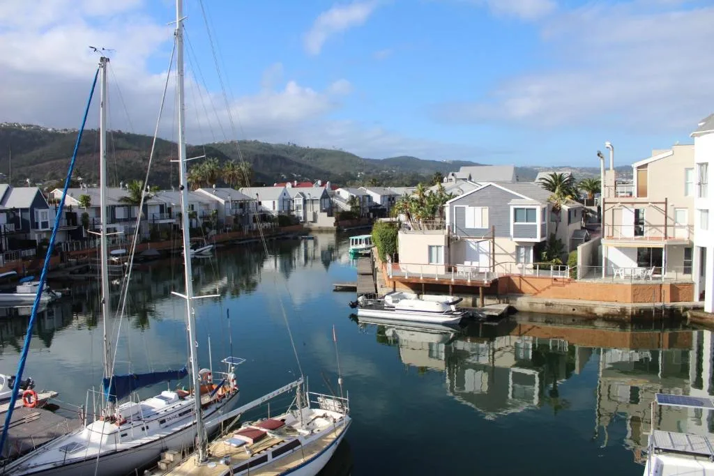 Tranquil lagoon view with sailboats, waterfront homes, and green mountains beyond