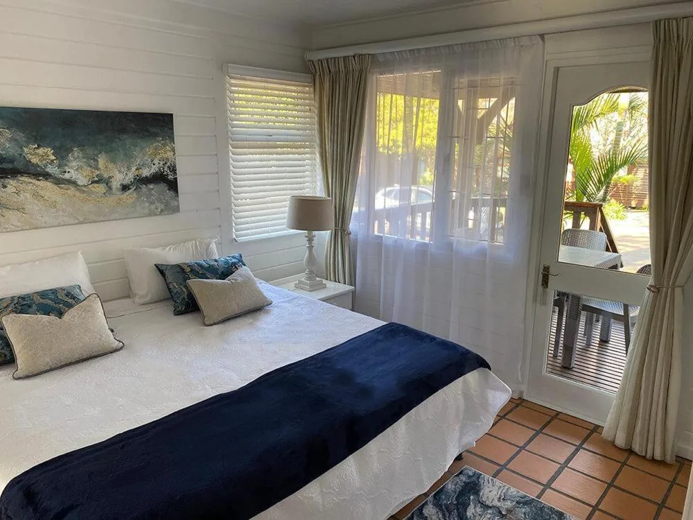 Bright bedroom with queen bed, ocean-themed artwork, and deck access doors