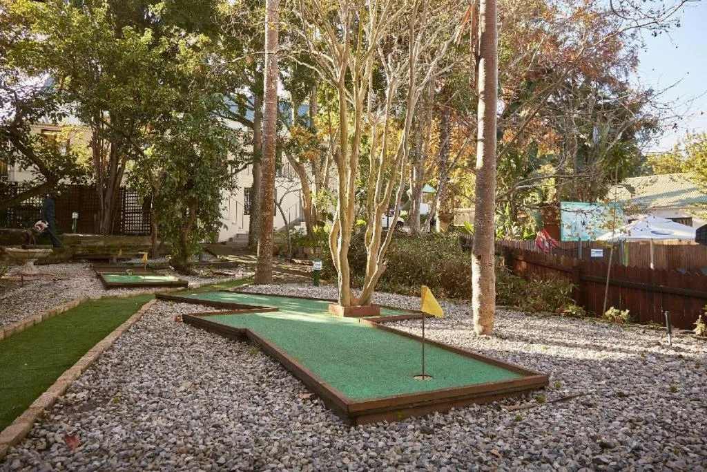 Miniature golf course with green fairways among tall trees and gravel