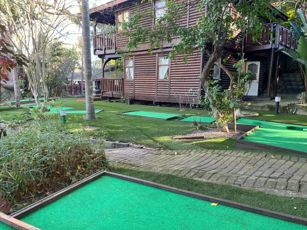 Mini golf course with multiple green holes and wooden chalet building