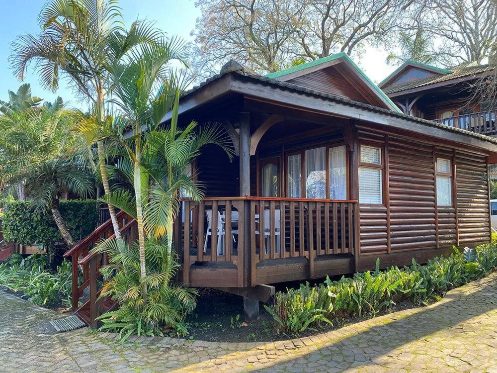 Wooden cabin with covered deck and tropical landscaping in garden setting