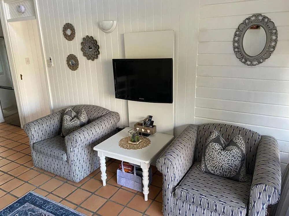 Bright lounge with patterned armchairs, wall-mounted TV, and decorative mirrors