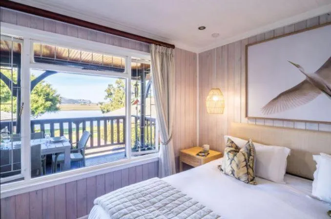 Bedroom with bed, river view through large windows, and waterfront deck access