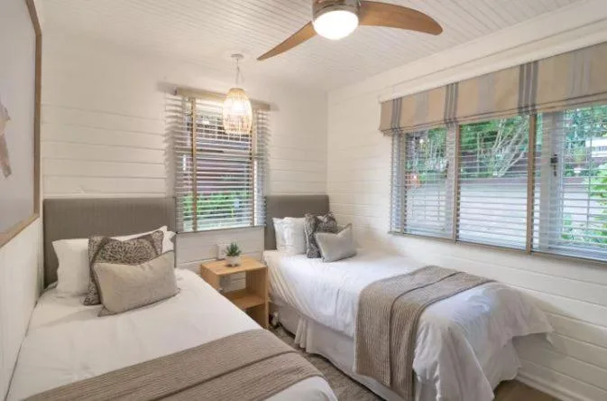 Bright bedroom with two twin beds, ceiling fan, and large windows overlooking garden