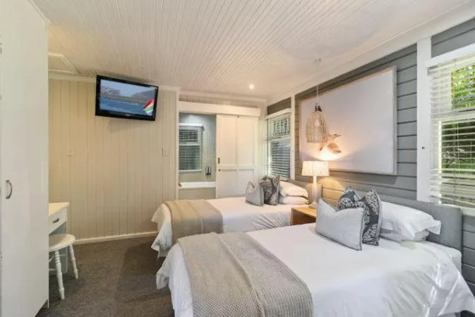 Spacious bedroom with two beds, wall-mounted TV, and bright windows