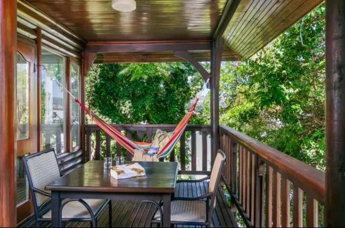 Covered timber deck with dining table, chairs, and relaxing hammock surrounded by lush greenery