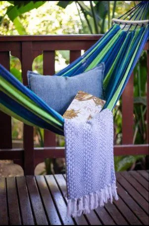Blue hammock with cushions and throw blanket on wooden deck
