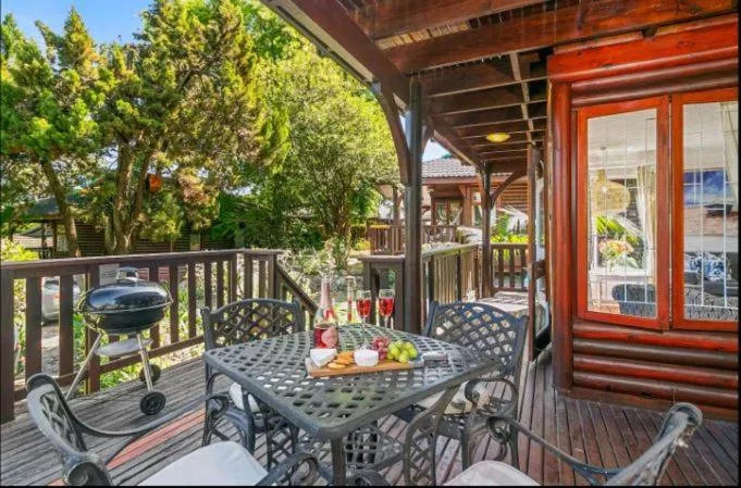 Covered deck with dining table, chairs, and braai grill overlooking garden