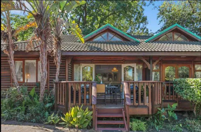 Charming wooden chalet with turquoise roof peaks and wide deck, surrounded by mature trees