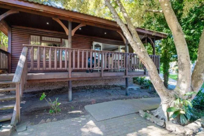 Wooden chalet with wraparound deck and mature trees, entrance area visible