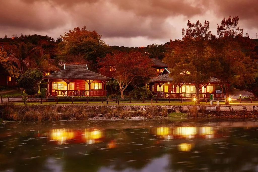 Riverside cottages lit at dusk, reflected in the Knysna River water below