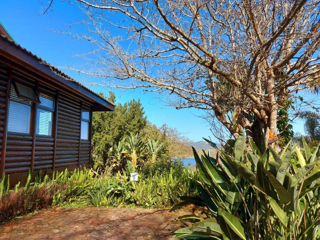 Modern wooden cabin with blue shutters overlooking water and lush gardens