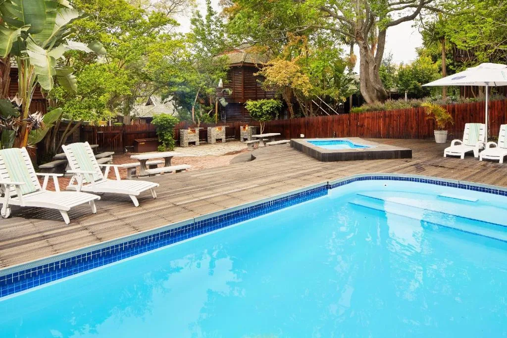 Sparkling blue swimming pool with wooden deck and white loungers, mature trees surrounding