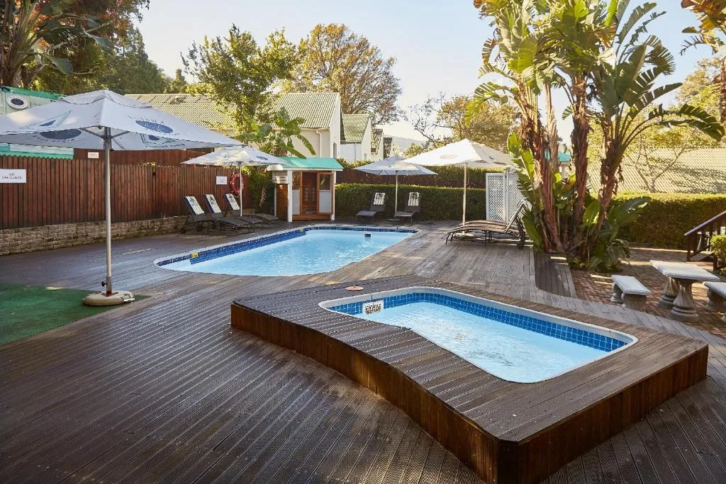 Two swimming pools with wooden deck, umbrellas, and tropical plants surrounding