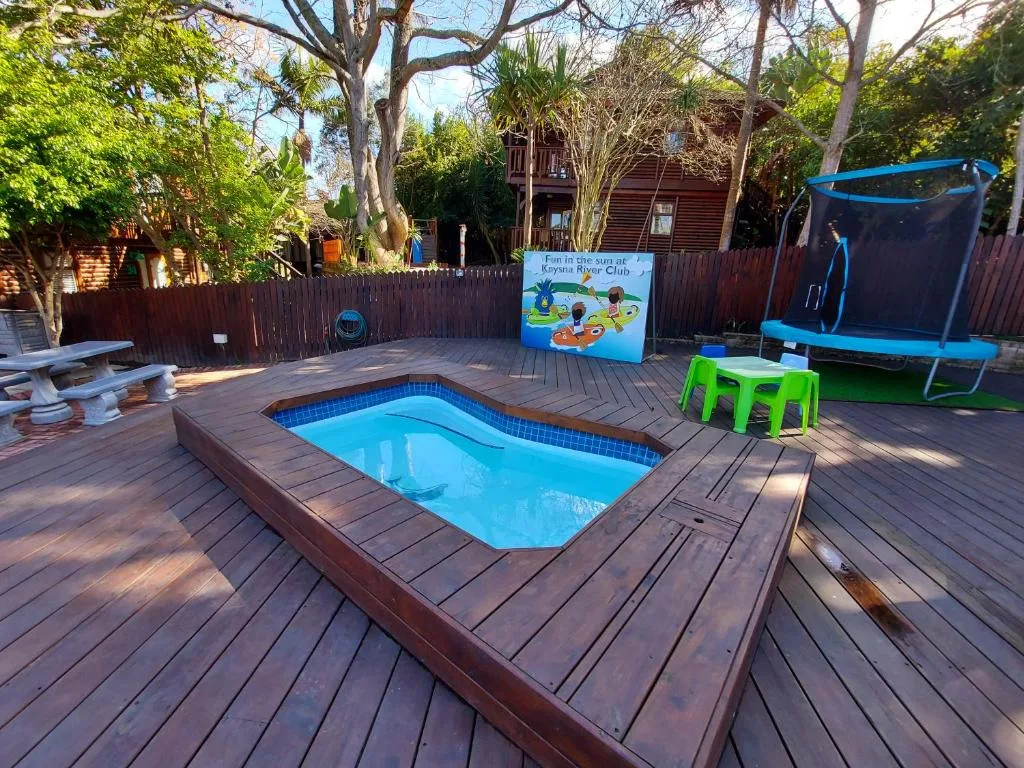 Rectangular swimming pool on wooden deck with trampoline and garden background