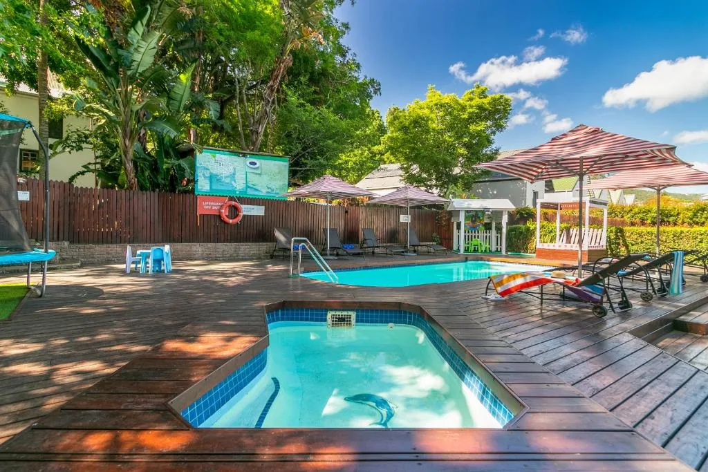 Twin swimming pools with loungers and shaded seating areas under umbrellas