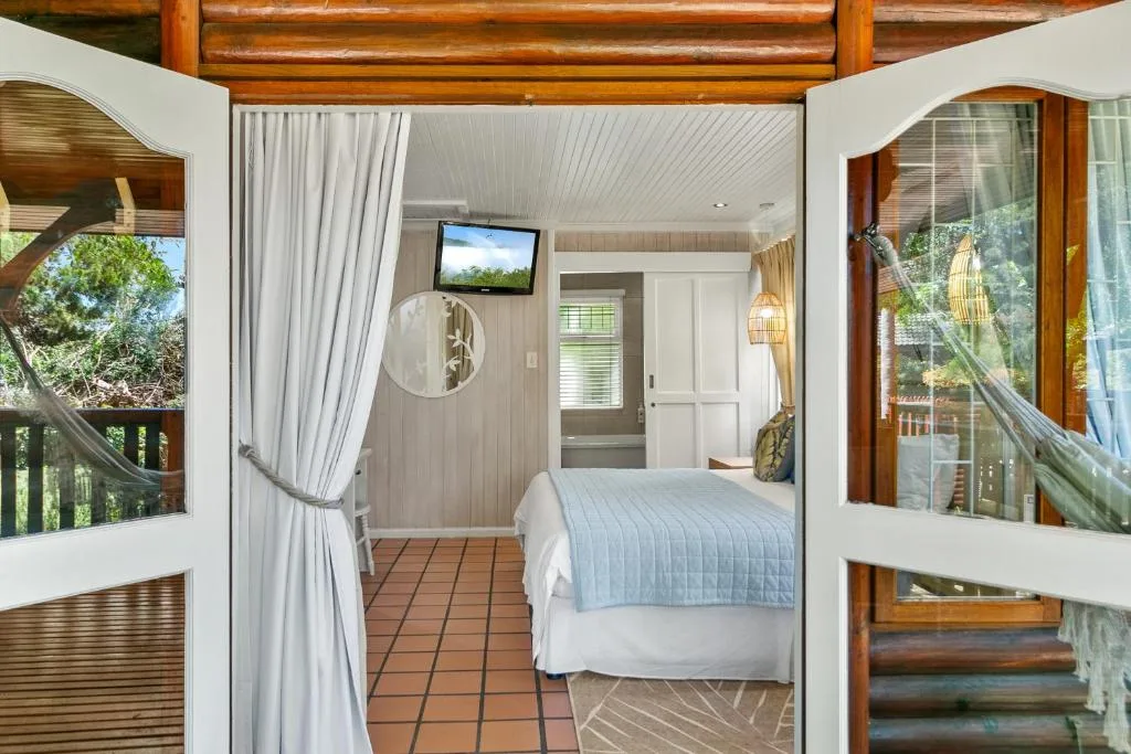 Bright bedroom with queen bed, terracotta floor, and large windows overlooking trees