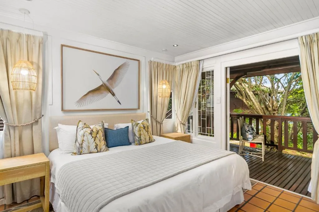 Bright bedroom with queen bed, large windows opening to tree-lined deck
