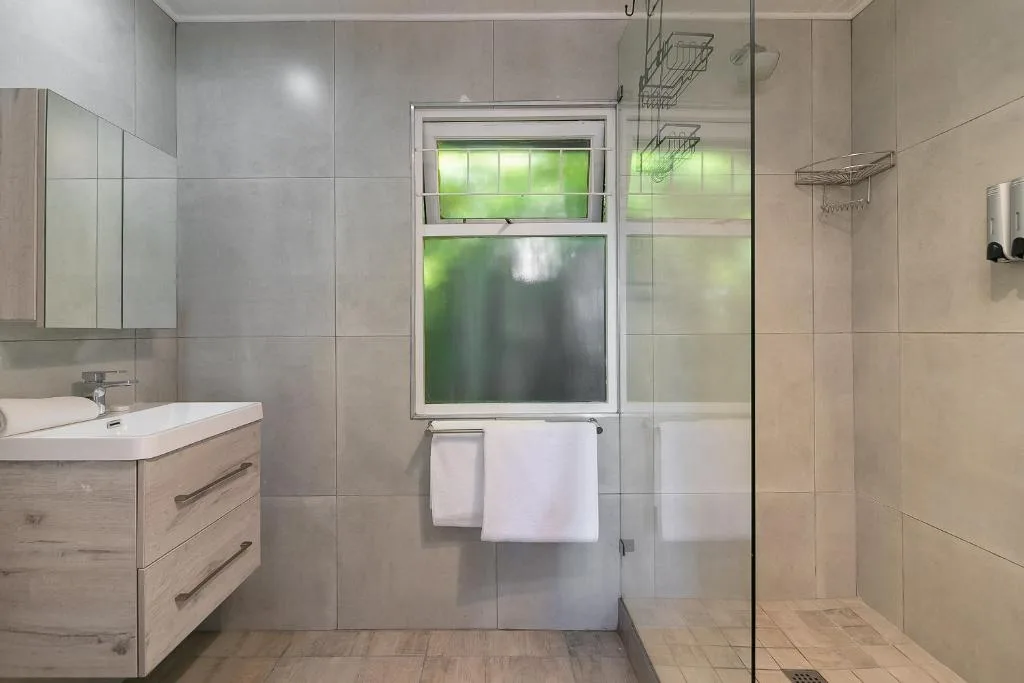 Modern bathroom with vanity, glass shower enclosure, and window overlooking garden