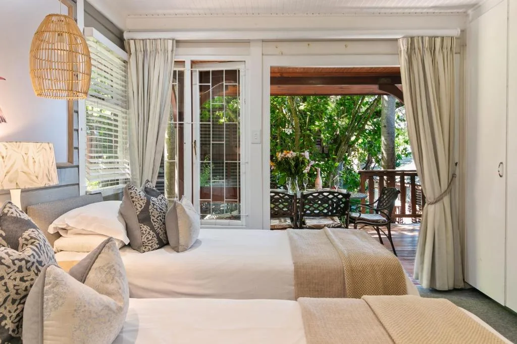 Bright bedroom with beds, woven lamp, and deck access overlooking gardens