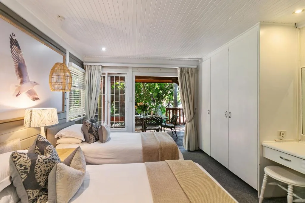 Bright bedroom with twin beds, deck access, and garden views through glass doors