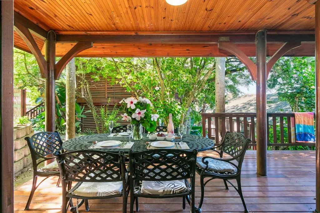 Covered wooden deck with dining table, chairs, and garden views