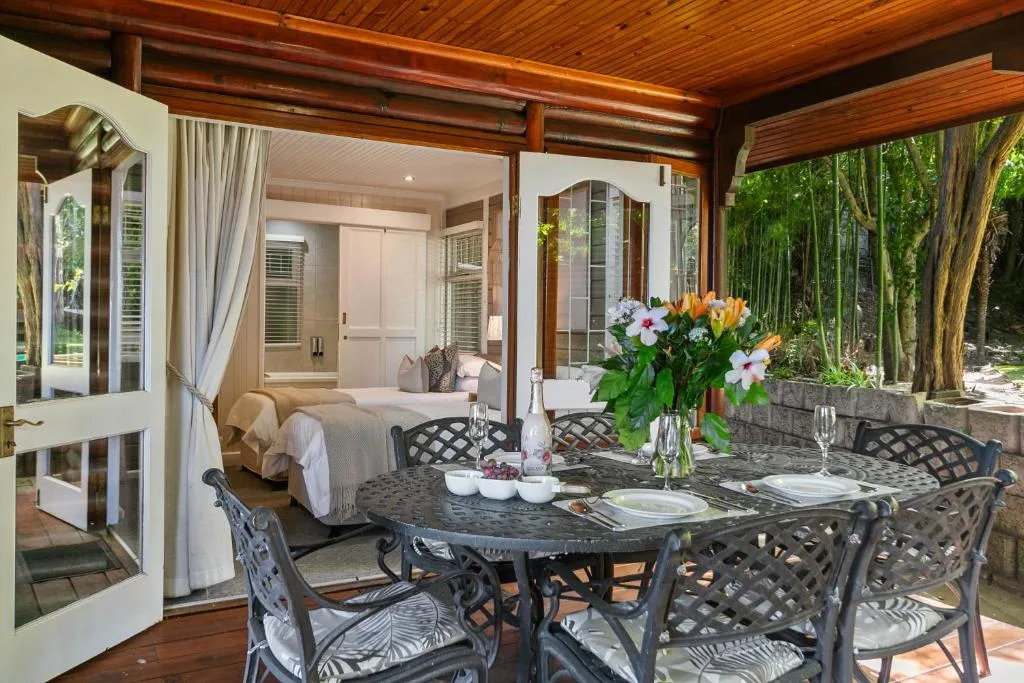 Covered deck with dining table, chairs, flowers, and forest views beyond