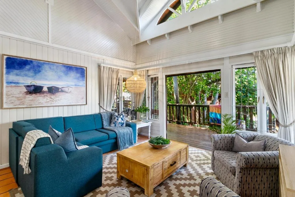 Bright open-plan lounge with teal sofa, wooden coffee table, and deck access