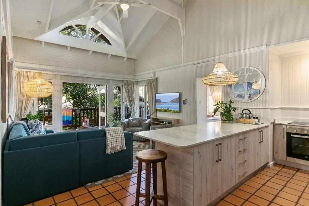 Open-plan living area with teal sofa, kitchen island, and ocean views through glass doors