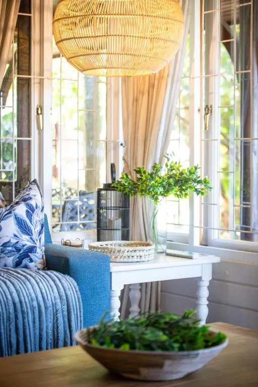 Bright lounge with woven pendant lamp, blue accents, and garden views through French doors