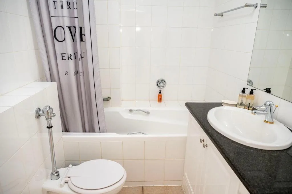Clean white tiled bathroom with toilet, vanity sink, and bathtub with shower
