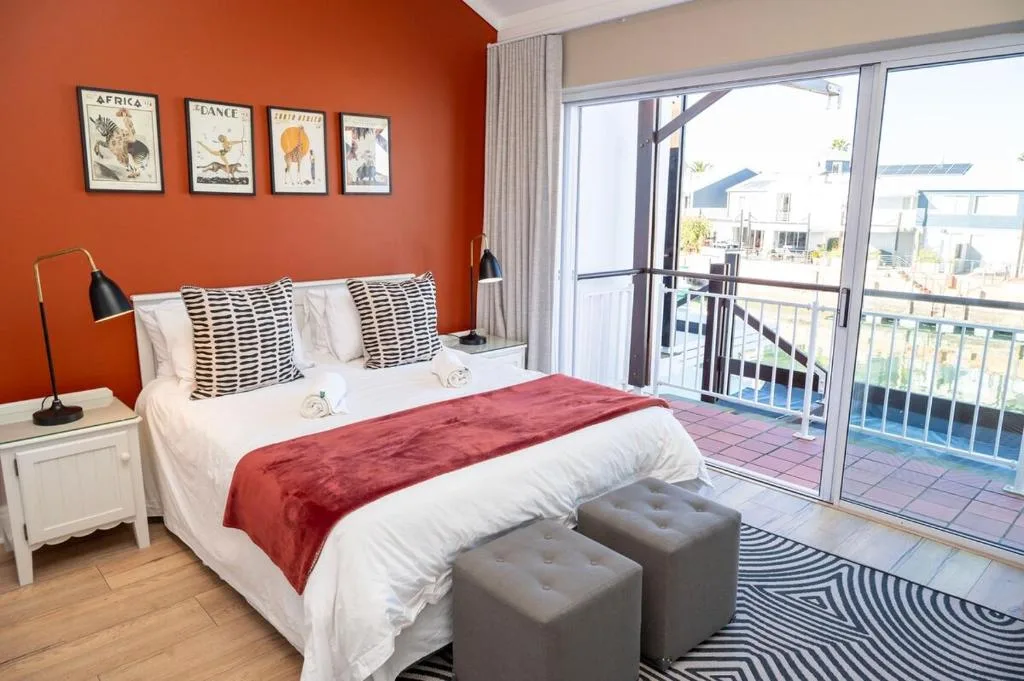 Bright bedroom with orange accent wall, queen bed, and balcony overlooking lagoon