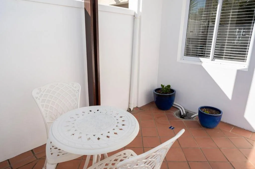 Compact outdoor patio with white chairs and potted plants, terracotta tiles