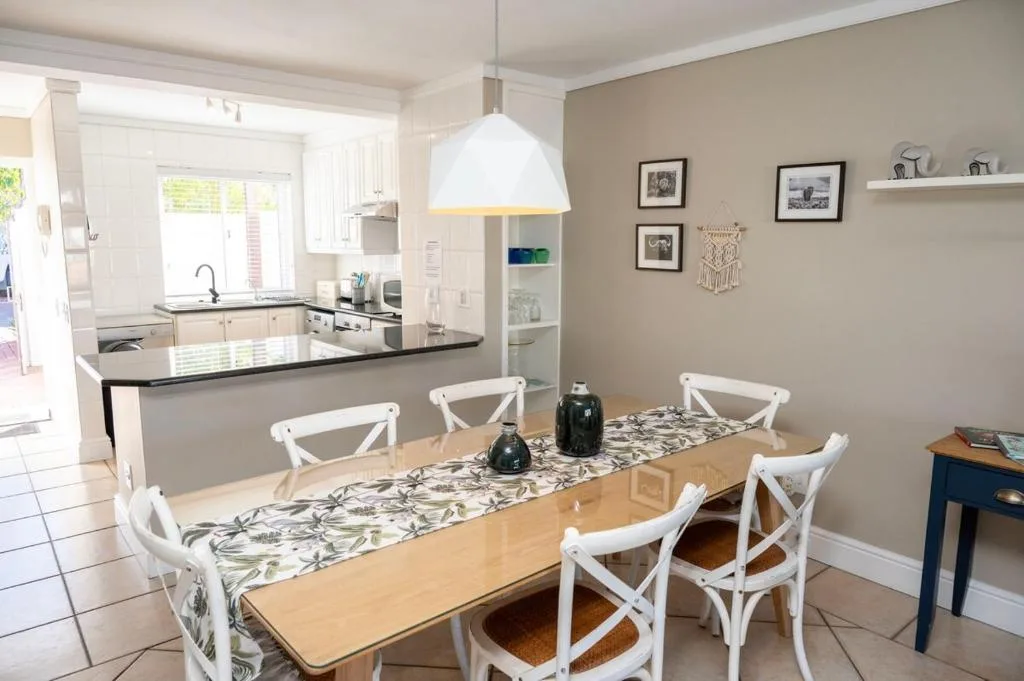 Bright dining area with wooden table, white chairs, and open kitchen view
