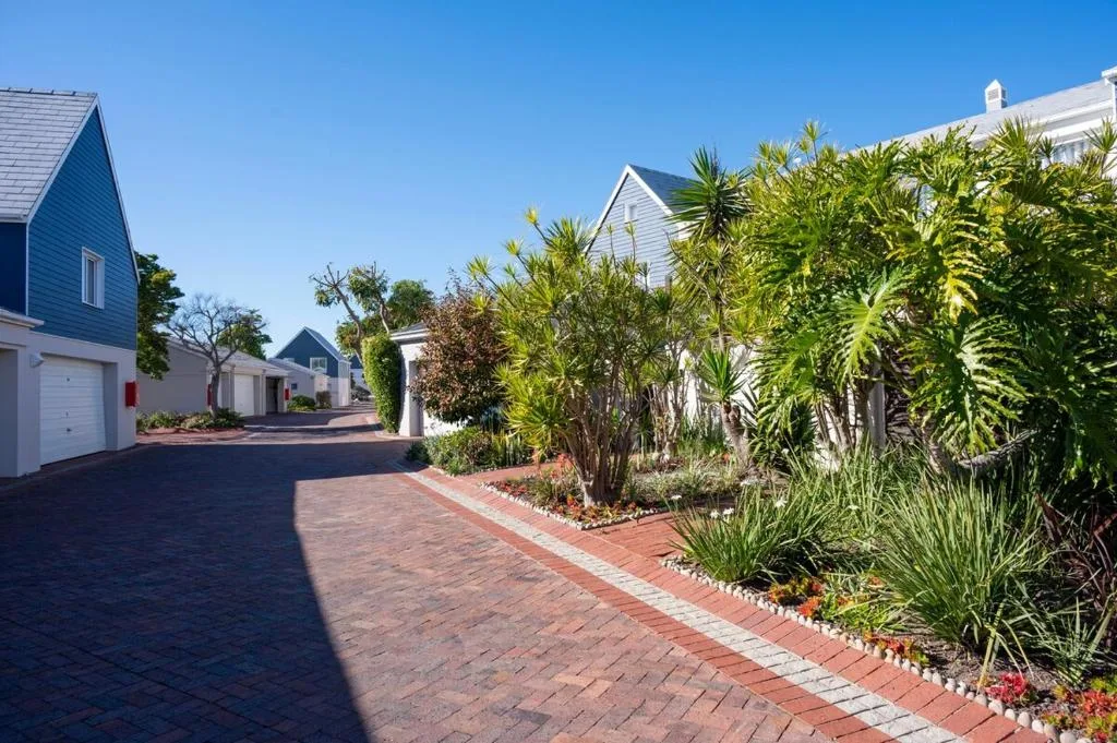 Brick driveway lined with tropical plants and white cottages with blue roofs
