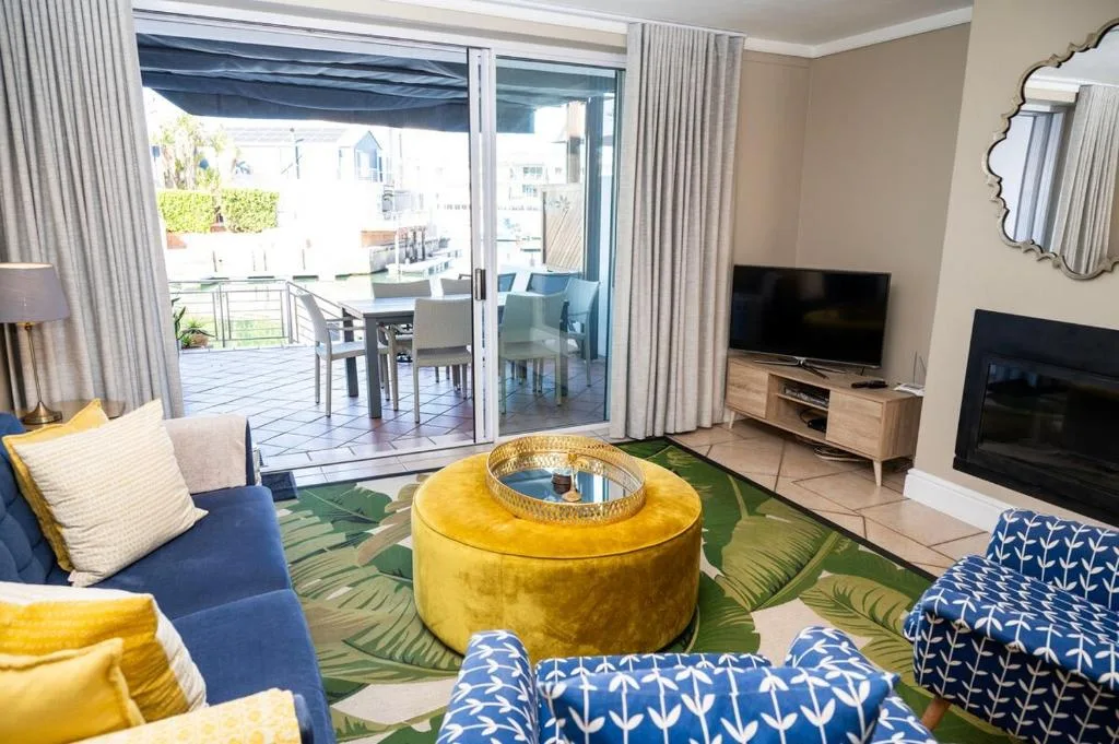 Bright lounge with colorful seating, TV, and deck access overlooking lagoon
